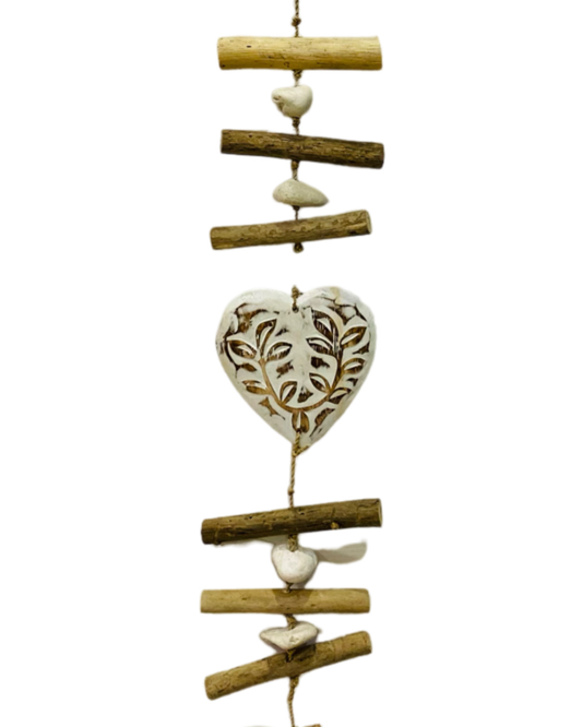 A wooden hanger with three white heart with brown patterned carving, pebbles and driftwood pieces.